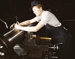 旋盤で加工されたM7戦車砲の砲身を、外側マイクロメータで計測する女性